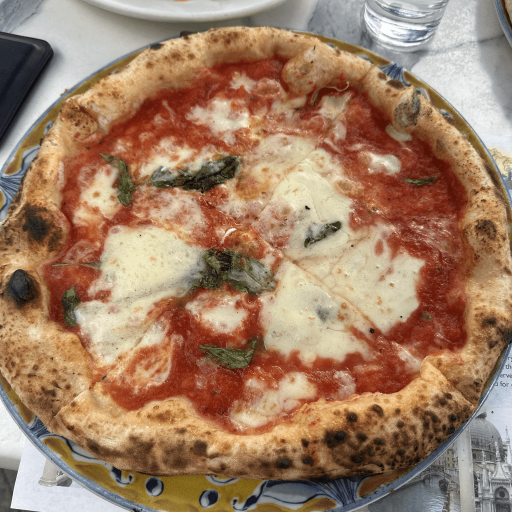 A freshly baked Neapolitan-style Margherita pizza sits centered on a decorative ceramic plate with a yellow rim and blue floral edge design, viewed from a slightly elevated angle.