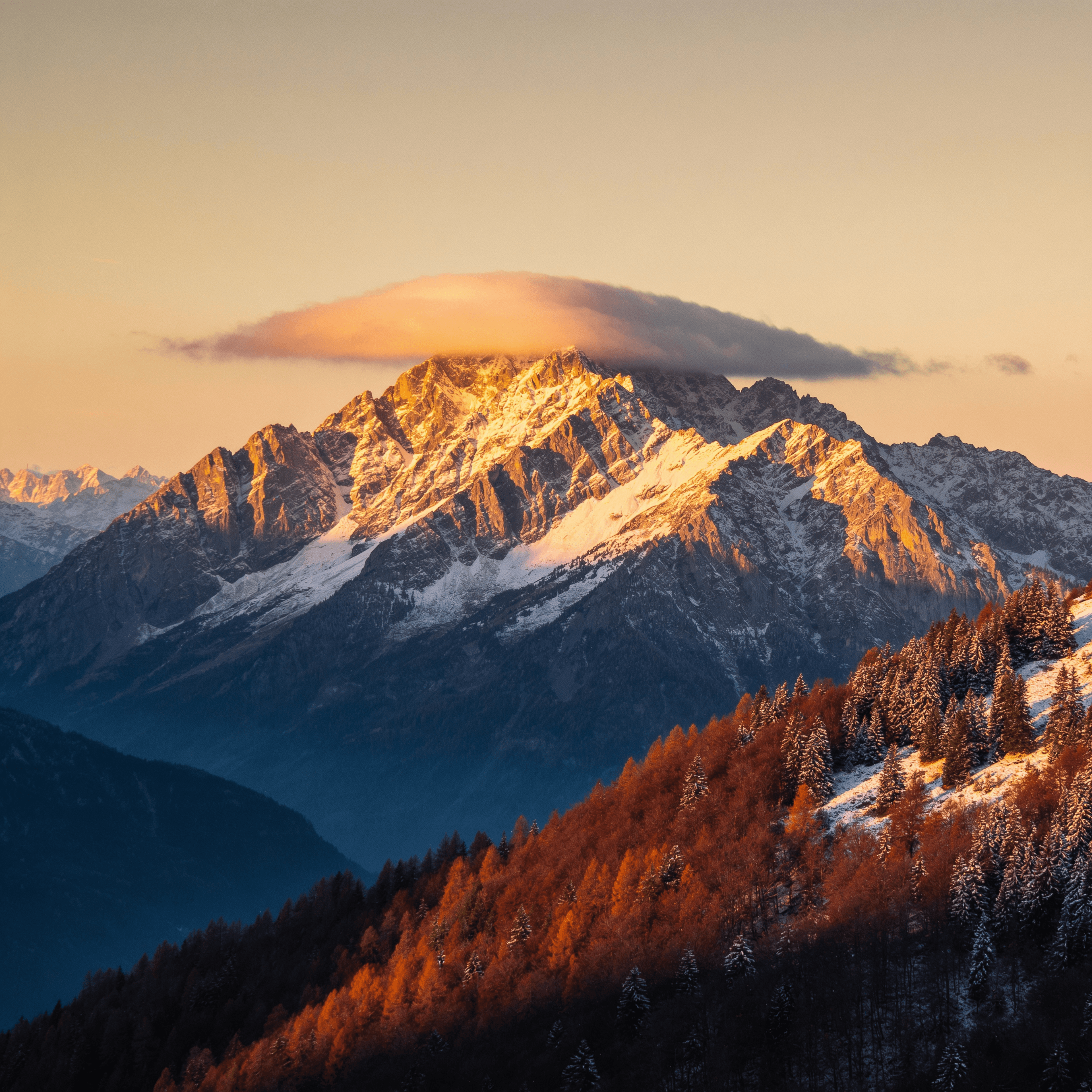 A rugged alpine mountain range stretches across the frame under a pale, softly graded sky that brightens toward the horizon, suggesting early morning or late afternoon light.