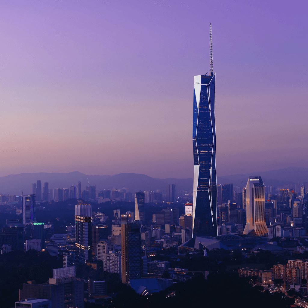 A wide city skyline at dusk fills the frame, with a tall, slender glass skyscraper slightly right of center dominating the composition and rising far above the surrounding buildings, its dark reflective facade edged by sharp white-lit lines and a thin spire extending into a clear purple-blue sky.