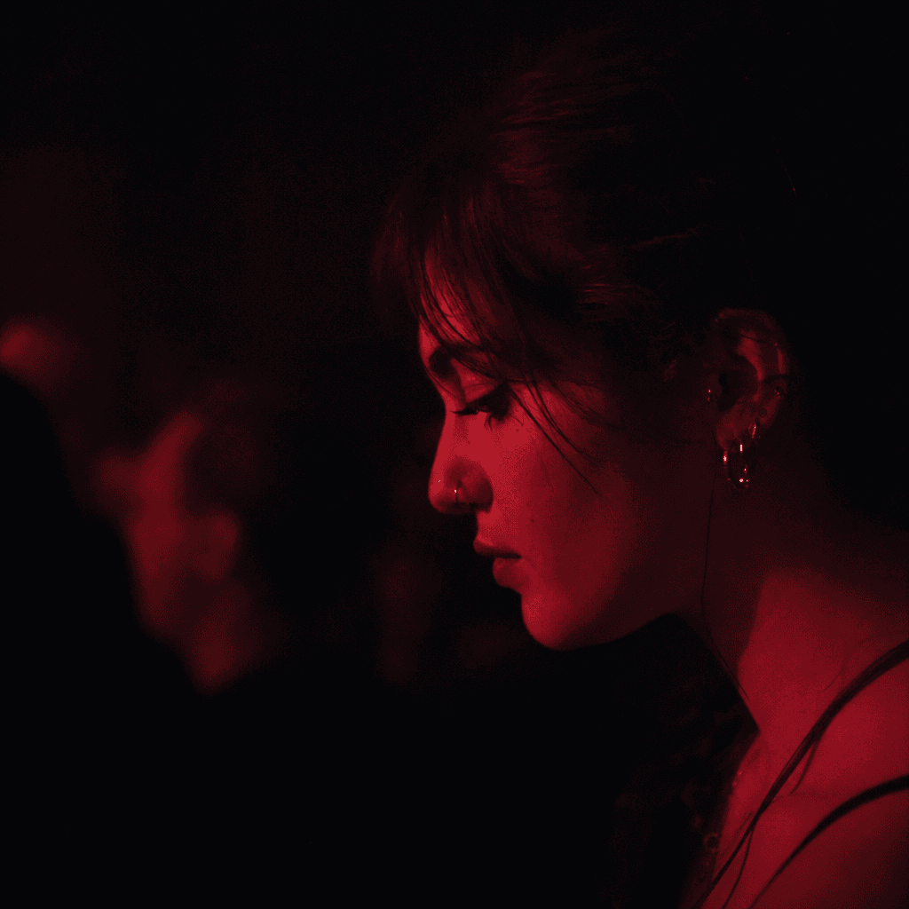 A very tight close-up shows a young woman’s face in profile turned slightly downward, filling the right half of the frame against a nearly black, indistinct background.