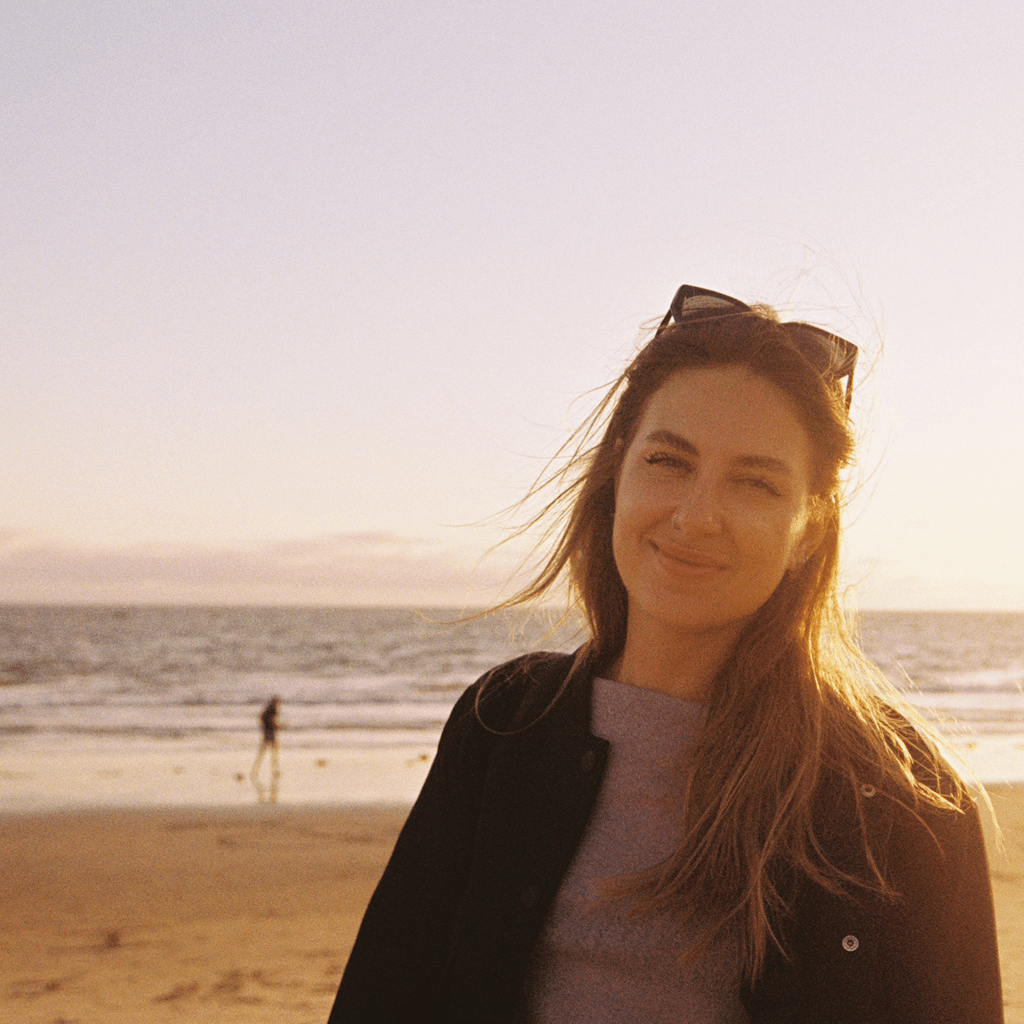 The scene is set outdoors on a beach during the early evening, with the sun dipping low on the horizon, casting a warm, golden glow over the sands.