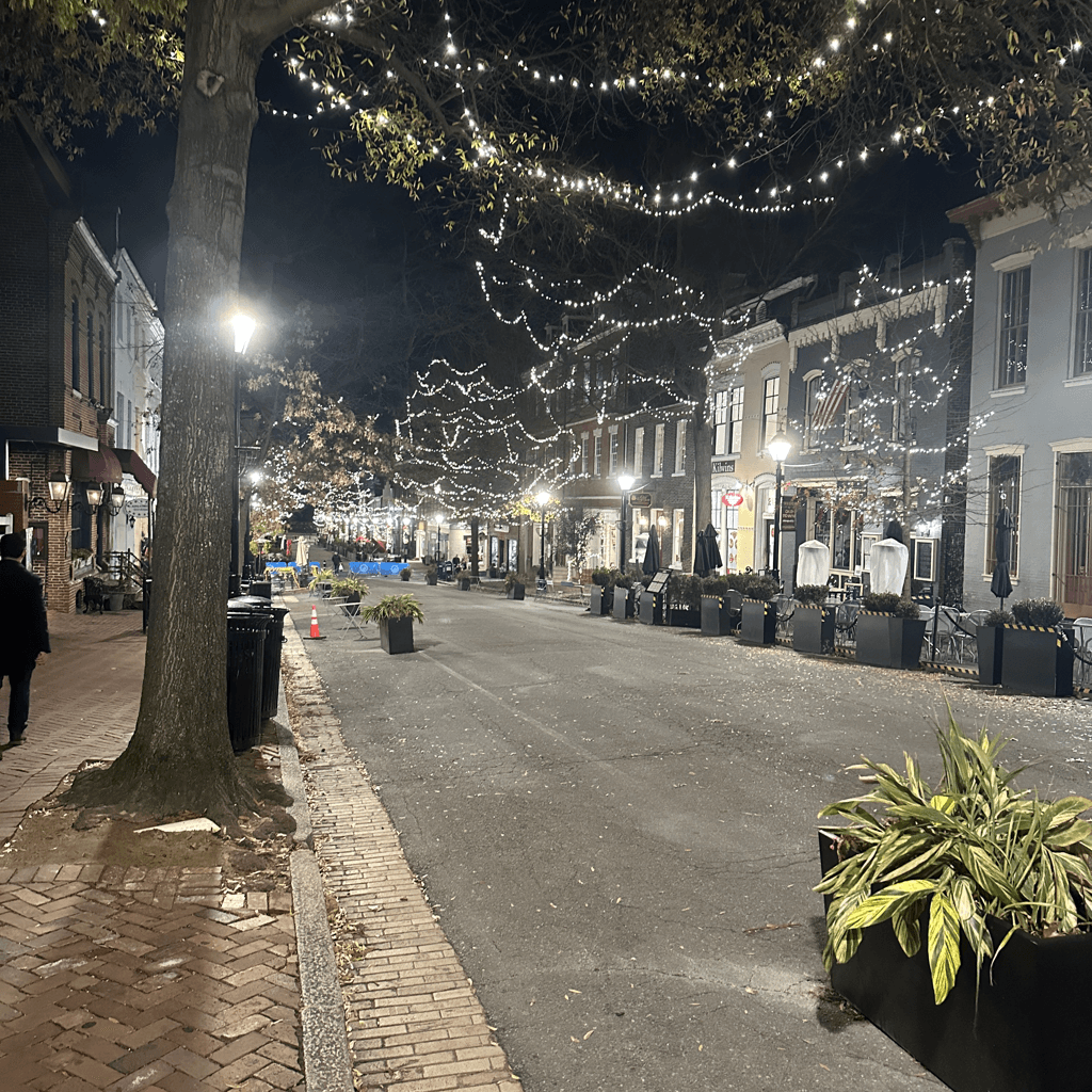 A quiet nighttime street scene captured at ground level looking down a paved roadway lined with brick-paved sidewalks and low-rise historic commercial buildings.