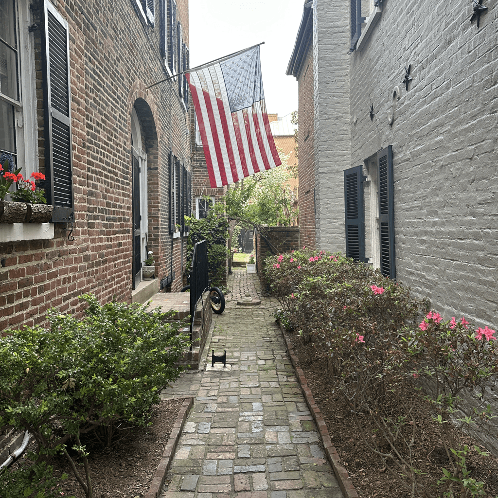 A narrow brick-paved alleyway recedes into the distance between two multi-story buildings, viewed from ground level looking straight down the passage.