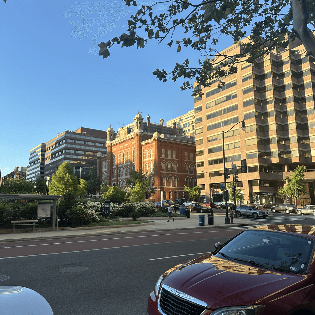 An urban street scene captured in late afternoon with warm, low-angle sunlight illuminating brick and glass facades against a clear blue sky.