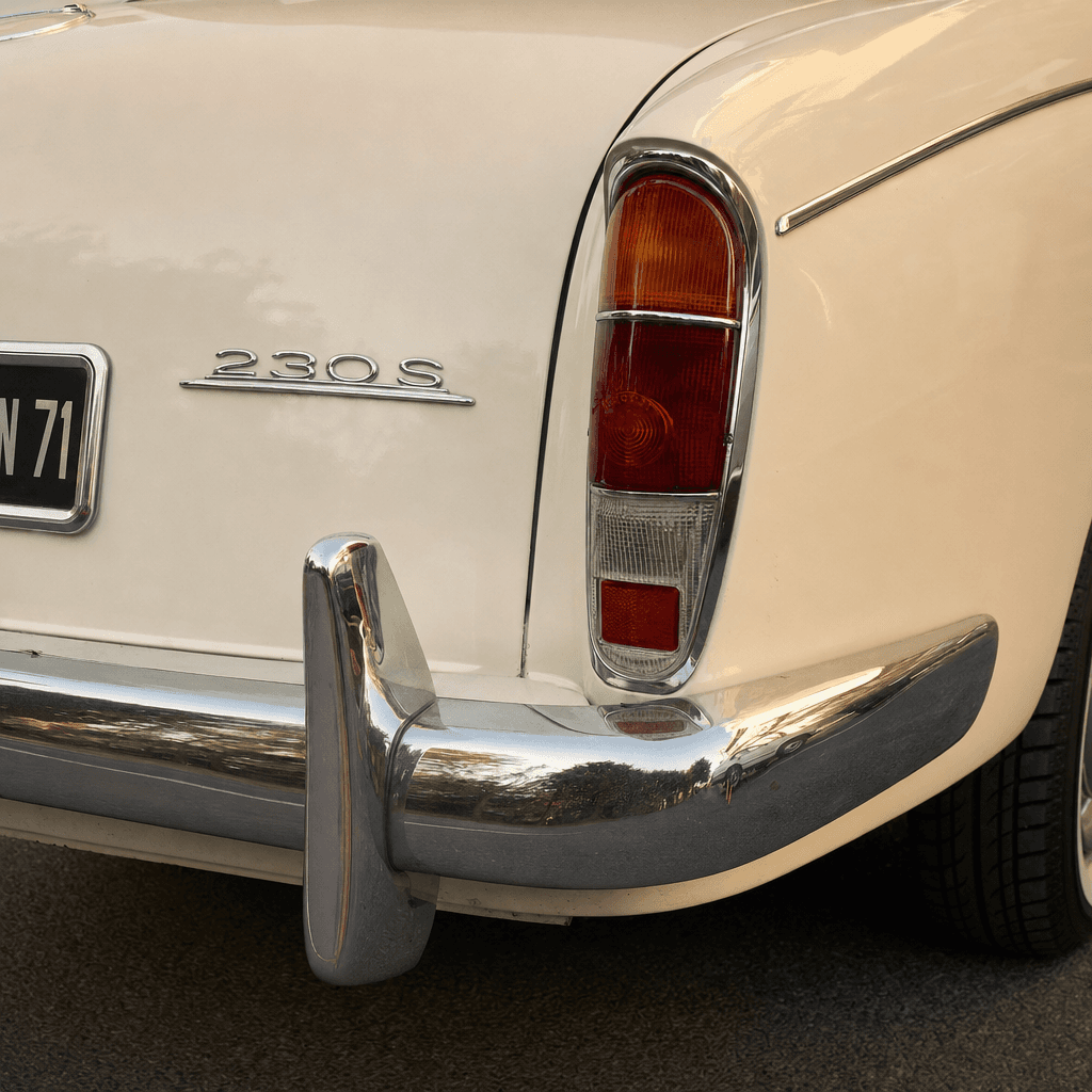 Close-up of the rear corner of a vintage cream-colored car, filling most of the frame at a slight downward angle.