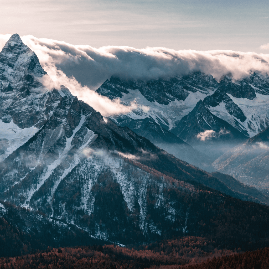 A rugged alpine mountain range stretches across the frame under a pale, softly graded sky that brightens toward the horizon, suggesting early morning or late afternoon light.