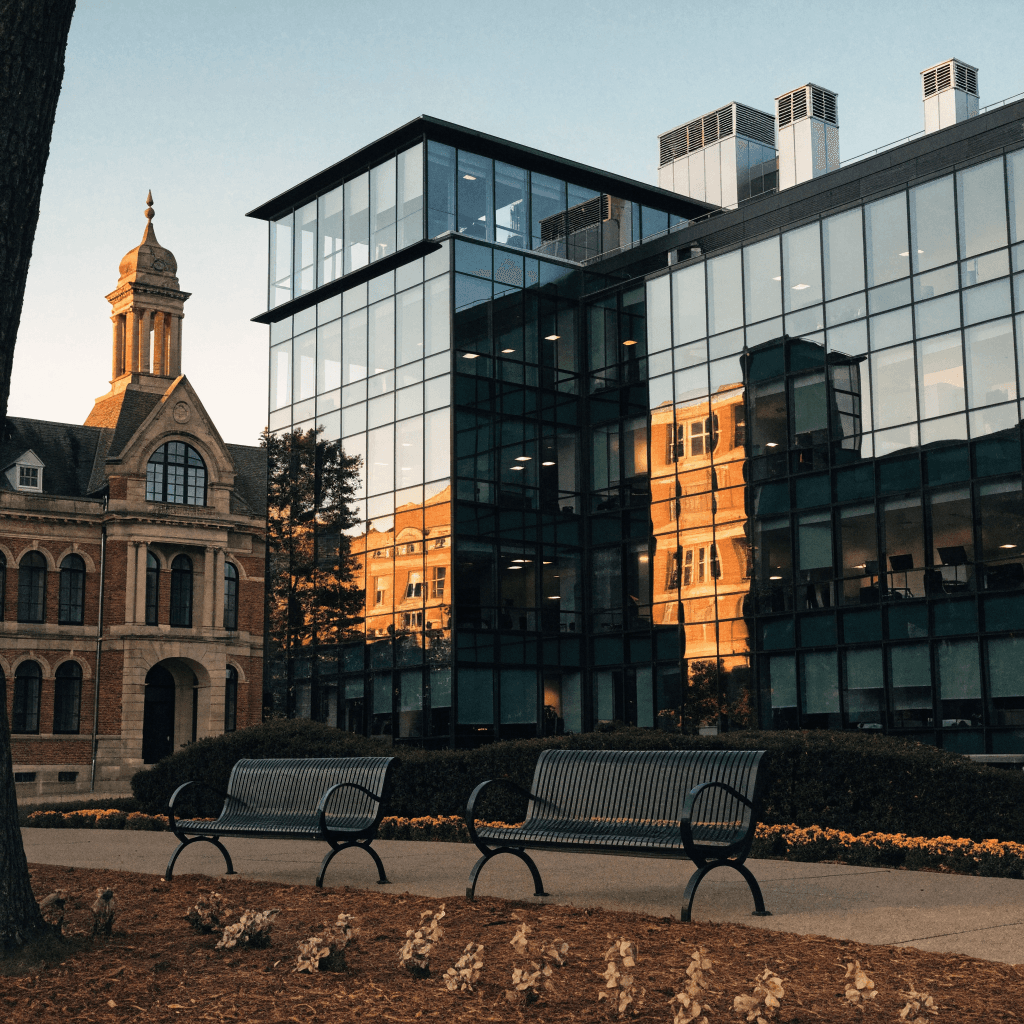 A modern multi-story building dominates the midground, its façade a grid of dark vertical mullions and reflective glass panels catching warm late-afternoon light, with rooftop vents and a glass-canopied section angling toward the right.