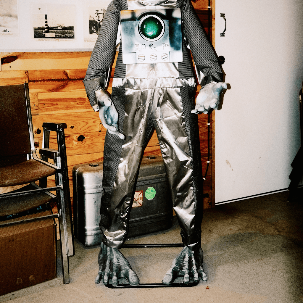A full-length novelty figure stands indoors against a mixed backdrop of wood paneling and a plain white wall, cropped at the neck and centered in the frame.
