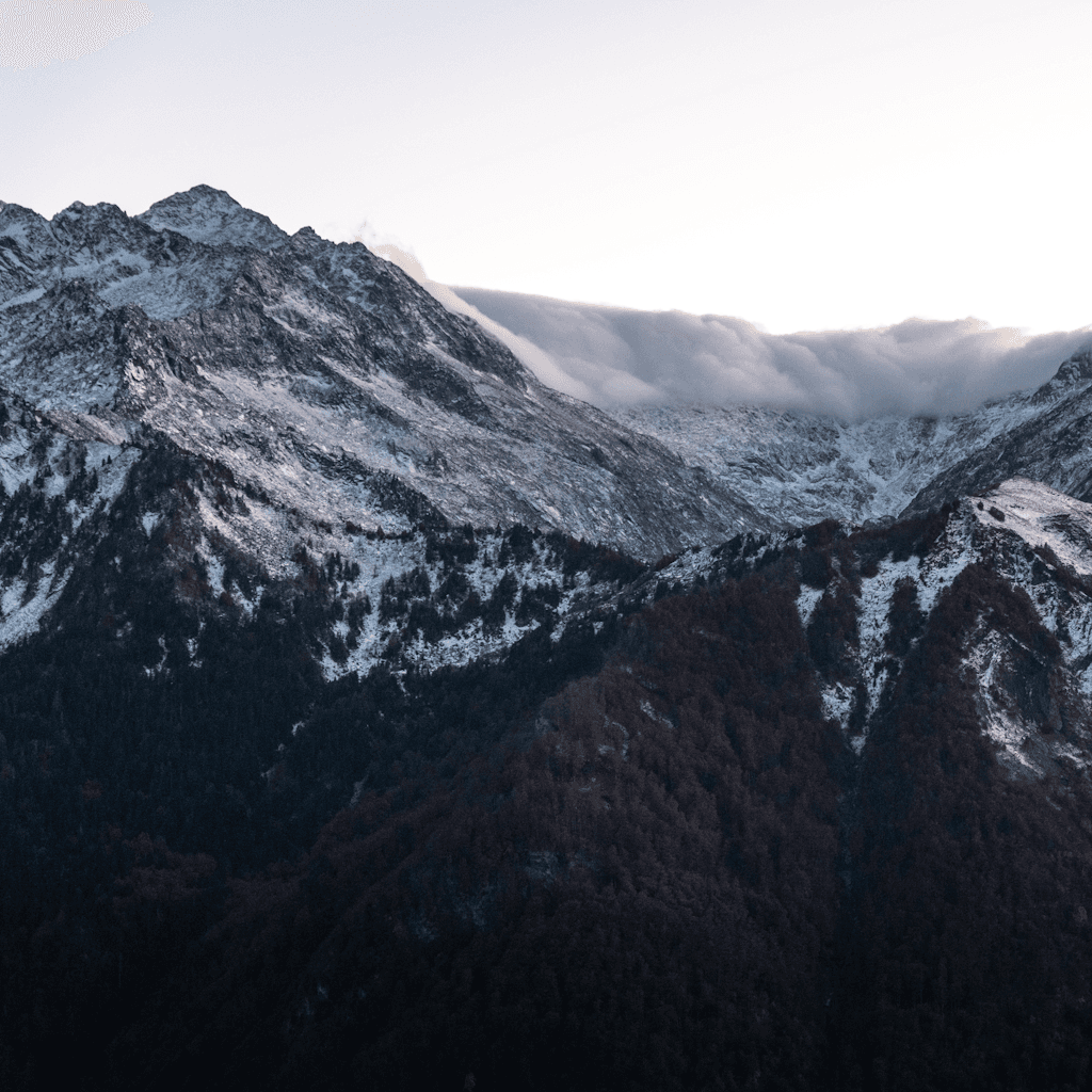 A rugged alpine mountain range stretches across the frame under a pale, softly graded sky that brightens toward the horizon, suggesting early morning or late afternoon light.